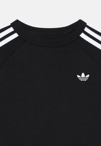 T-shirt preta de algodão com gola redonda, apresentando três riscas brancas nos ombros e um pequeno logótipo branco no peito.