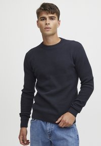 Pull bleu marine avec un motif en tricot gaufré texturé, poignets et ourlet côtelés, col rond, accompagné d'un jean en denim bleu clair.