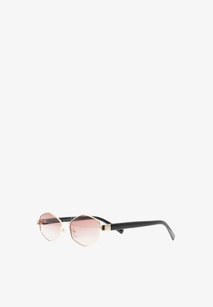Occhiali da sole esagonali con montatura in metallo dorato, lenti a gradiente rosa e bracci neri curvi appoggiati su una superficie bianca.