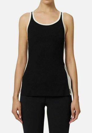 Donna che indossa una canottiera nera senza maniche con rifiniture bianche e pantaloni neri coordinati, in piedi contro uno sfondo chiaro e uniforme.