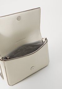 Bolso bandolera de Calvin Klein Jeans, en suave cuero sintético beige texturizado, con cierre a presión, herrajes plateados, interior con forro de tela gris y bolsillos.