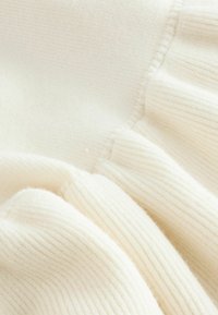 Primer plano de tela de punto acanalado suave en color crema con detalles de textura plegada y recogida.