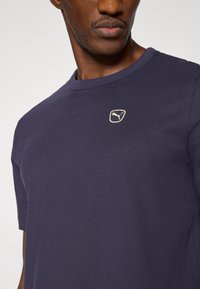 Μπλε βαμβακερό μπλουζάκι σε ναυτικό χρώμα με στρογγυλή λαιμόκοψη, κοντά μανίκια και μικρό ανοιχτ όχρωμο λογότυπο στο στήθος. Ομαλή υφή.