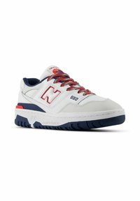 Baskets en cuir blanc avec des accents rouges et navy, présentant une surface texturée, une languette rembourrée et une semelle en caoutchouc avec un motif de crampons.