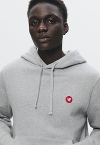 Svetlošedá mikina s klokaním vreckom a malým červeným kruhovým logom s bielym "W". Mäkkučký materiál, nastaviteľné šnúrky.