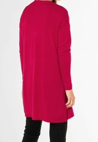 Långärmad tunika i livlig magenta, tillverkad av mjukt tyg med en avslappnad, lös passform, med rund halsringning och sidofickor.