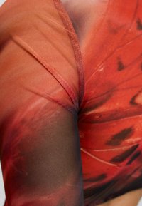 Gennemsigtig langærmet top med et gradient i orange og røde nuancer, med en mesh-struktur og et abstrakt mønster, der blander sig med mørke kanter.