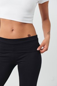 Juodos sportinės legging'ės su plačiu juosmeniu, lygia textura ir prigludusia forma. Derinamos su baltu trumpu topu, atidengiančiu pilvą.