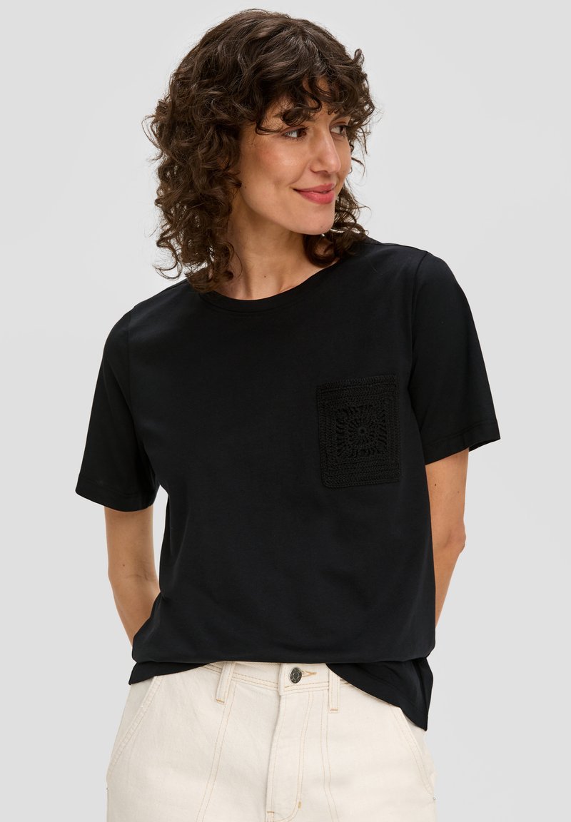 Zwarte katoenen T-shirt met korte mouwen, voorzien van een gehaakte pocket aan de linkerkant. Rechte snit, losse pasvorm.