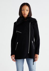 Čierny vlnený kabát s golierom z umelého kožušiny, asymetrickým zipsom a dvojicou predných vreciek na zips. Dlhé rukávy s hladkou textúrou.