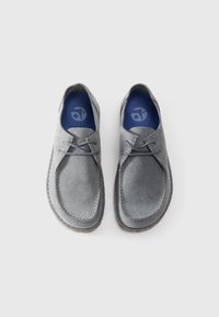 Chaussures en suède gris avec un bout arrondi, un laçage et une semelle intérieure bleue contrastante. La semelle est marron avec une finition texturée.