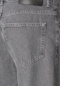 Grå denim jeans med en baklomme med et enkelt klaffedesign, synlige sømmer og en lett teksturert finish. Svart livsdetalj.