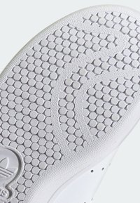 Primo piano di una suola di scarpa bianca con un motivo di battistrada circolare e linee curve testurizzate per la presa, con il logo Adidas vicino al tallone.