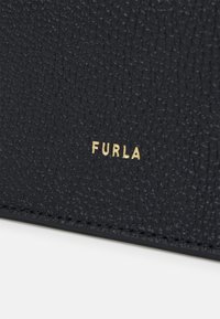 Zbliżenie na skórę o fakturze czarnej z małym, złotym logo marki "FURLA" wytłoczonym blisko szwu.