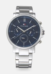 Montre en acier inoxydable argentée avec un cadran bleu marine, trois sous-cadrans, index horaires argentés et bracelet en métal ajustable.