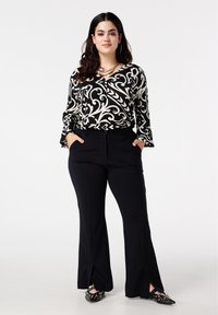 Zwart-wit gebloemde blouse met uitlopende mouwen, gecombineerd met zwarte high-waisted broek met zijopeningen. Schoenen met band en studs.