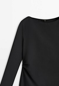 Haut noir à manches longues avec un col bateau, confectionné en tissu lisse. Le design présente un drapé léger sur les côtés pour plus de détail.