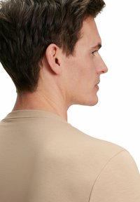 Beige t-shirt met een ronde halslijn, korte mouwen en een zachte, gladde textuur, zijaanzicht weergegeven met minimale details.