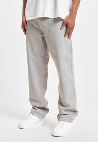 Pantalones vaqueros de mezclilla gris claro con un ajuste relajado, que cuentan con bolsillos laterales y costuras en contraste. Se llevan con zapatillas blancas.