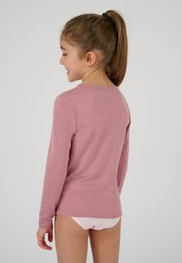 Maglietta a maniche lunghe in morbido tessuto rosa, scollatura tonda, vestibilità aderente, texture liscia, abbinata a biancheria intima rosa chiaro. La vista dal retro mostra la lunghezza delle maniche.