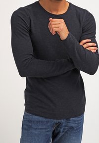 Långärmad, rundhalsad tröja i mörkgrått, tillverkad av mjukt material. Figursydd design med minimala sömmar, kombinerad med blå denimjeans.