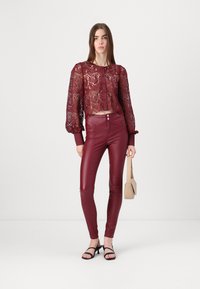 Burgundy lace cropped blouse with long puff sleeves and buttons, paired with tight burgundy leather-like pants and black strappy sandals.