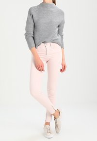 Suéter gris de punto, jeans rosa ajustados con cremalleras en los tobillos y zapatillas beige. El conjunto está dispuesto sobre un fondo neutral.