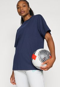 Marinblå bomullströja med korta ärmar, hålls med en svartvit mönstrad fotboll med röda accenter.
