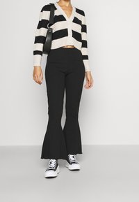 Černobílý pruhovaný krátký kardigan na knoflíky, kombinovaný s černými žíhanými rozšířenými kalhotami a černo-bílými teniskami.