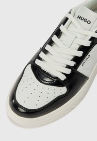 Sneaker in pelle bianca e nera con punta perforata, lacci bianchi, linguetta imbottita e dettaglio del logo sul lato.