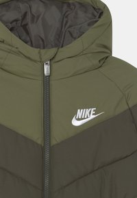 Chaqueta acolchada Nike de color verde oliva con capucha, cremallera central y logo de Nike bordado en blanco en el pecho.