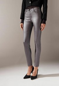 Jeans skinny grigio metallico con vestibilità slim, cuciture a contrasto, tasche frontali e vita media, abbinati a scarpe nere con tacco alto.