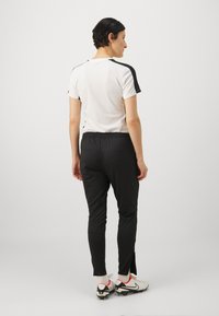 Športový outfit s bielym tričkom s krátkym rukávom a čiernymi detailami, čiernymi zúženými nohavicami. Topánky sú biele s červenými detailmi a čiernymi podrážkami.