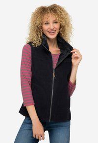 Granatowa bezrękawnik z zapięciem na zamek, pluszowym kołnierzem i kieszeniami bocznymi, noszony na różowej i szarej bluzie z długim rękawem w paski.
