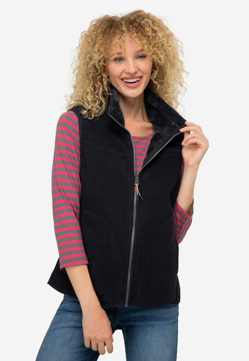 Granatowa bezrękawnik z zapięciem na zamek, pluszowym kołnierzem i kieszeniami bocznymi, noszony na różowej i szarej bluzie z długim rękawem w paski.