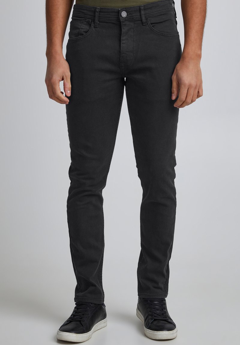 Svarte, smale jeans laget av denim, med fem lommer, beltestropper i midjen og en jevn tekstur. Brukes med svarte joggesko.