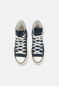 Zapatillas altas de lona azul marino con un diseño de cordones blancos, que presentan patrones de estrellas en la parte superior y una puntera de goma blanca.