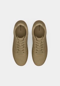 Ζευγάρι μπεζ σπορ παπούτσια με κορδόνια, με διάτρητη περιοχή στο μπροστινό μέρος και εσωτερικές σόλες με λογότυπο, φωτογραφημένα από ψηλά σε λευκό φόντο.
