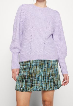 Kvinde iført en lavendelfarvet strikket sweater med puffede ærmer og et højtaljet mininederdel i tern i blå, grønne og sorte toner.