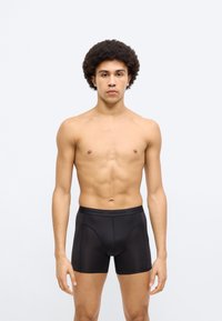 Μαύρα αντρικά μπλεζέρ με ομαλή υφή, ελαστική μέση και αντίθετες ραφές, φορεμένα από μοντέλο χωρίς πουκάμισο.