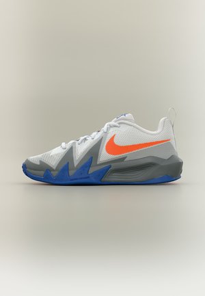 Chaussure de sport blanche et grise avec un swoosh Nike orange vif et un détail de semelle en zigzag bleu, montrée de profil sur fond uni.