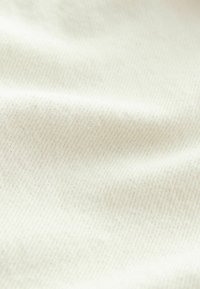 White cotton fabric with a smooth texture, featuring a fine, diagonal weave pattern. Subtle, natural speckles are visible throughout.