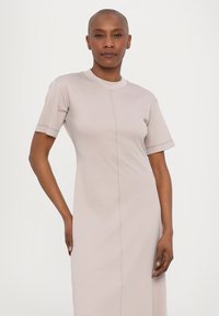 Valaistusvaalean beige lyhythihainen mekko, jossa on yksinkertainen siluetti. Mekossa on näkyvä kes seams ja pyöreä pääntie, ja se on valmistettu pehmeästä kankaasta.