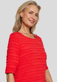 Rotes Kurzarmoberteil mit strukturiertem, geschichteten Design. Verfügt über einen runden Ausschnitt und einen weichen, leichten Stoff.