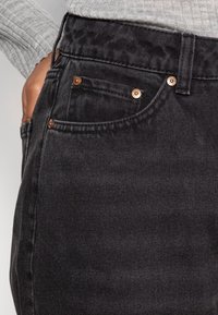 Černé džíny z denimu mají klasický pětihybridní design, měděné akcenty a jemnou texturovanou úpravu v oblasti pasu.