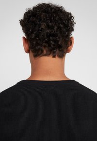 Black ribbed knit sweater with a round neckline, shown from the back, highlighting short curly hair and textured fabric.