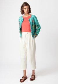 Cárdigan de color turquesa con un patrón sobre una blusa coral, combinado con pantalones de pierna ancha crema y sandalias marrones. Tejido texturizado y colores vibrantes.