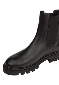 Bottine en cuir noir avec panneaux latéraux élastiques et semelle en caoutchouc texturé présentant des rainures profondes pour une meilleure adhérence. Design à bout arrondi.