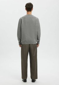 Hall hall värviga kudumisega kampsun pikkade võlgadega, soonikkõrvalpiid ja ümara kaelusega, millele on lisatud pruunide ruuduliste laiade pükstega ja mustade kingadega.