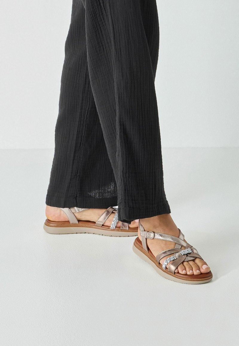 Sandales à brides en argent métallique et beige, avec des brides croisées, une boucle réglable et une semelle en caoutchouc marron clair.